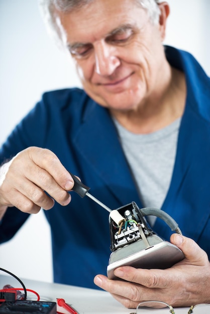 Старший взрослый электрик проверяет и ремонтирует старый утюг.