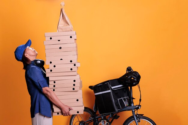 Senior afhaalmaaltijden staan met eten bestellen en pizzadozen vasthouden, pizzeria-service. Restaurantkoerier die afhaalmaaltijden vervoert met fiets op gele achtergrond. Afhaalconcept