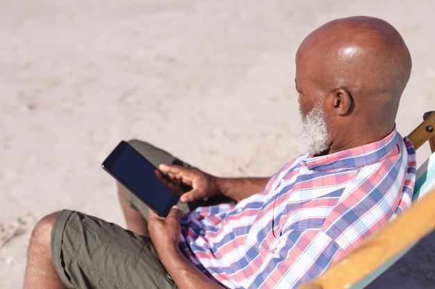 Senior african american man using digital tablet at the beach. travel vacation retirement lifestyle concept