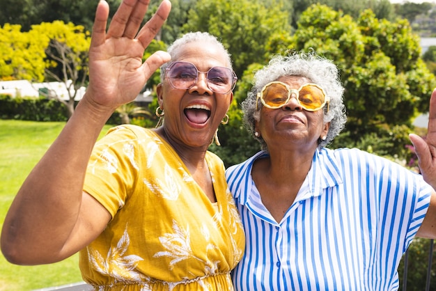 Senior African American woman and senior biracial woman are waving with bright smiles