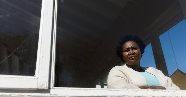Senior african american woman spending time at home, looking through window. isolating during coronavirus covid 19 quarantine lockdown.