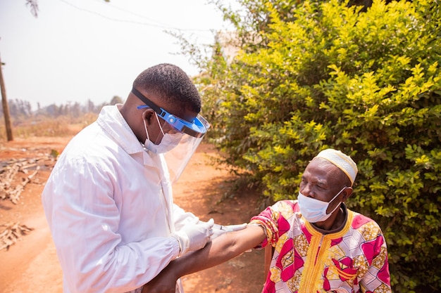 Uomo africano anziano che viene vaccinato all'aperto durante l'era della pandemia di covid19