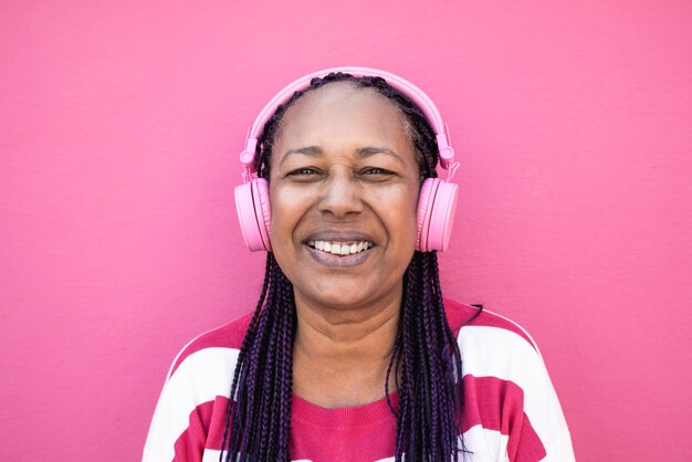 Senior african woman listening playlist music with headphones - Focus on face