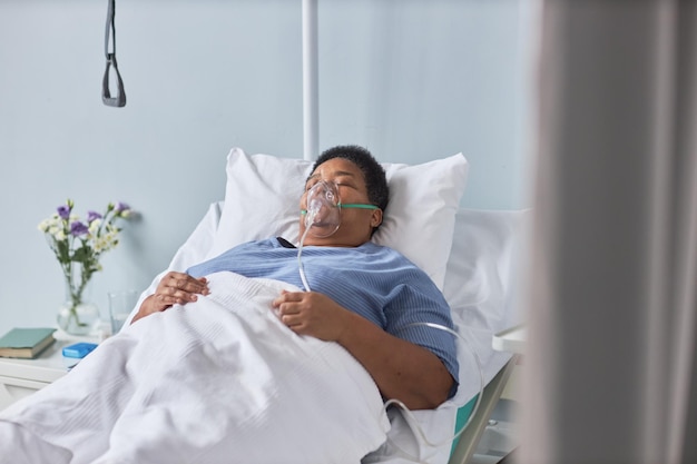 Senior Afro-Amerikaanse vrouw die op bed ligt in een ziekenhuiskamer met zuurstofondersteuning