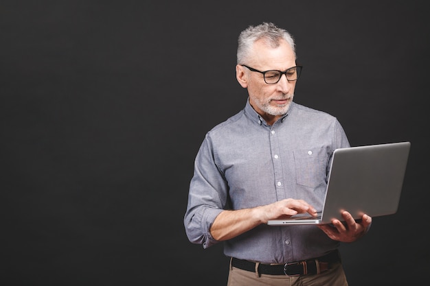 Senior aged bearded old man in eyeglasses holding laptop computer and smiling