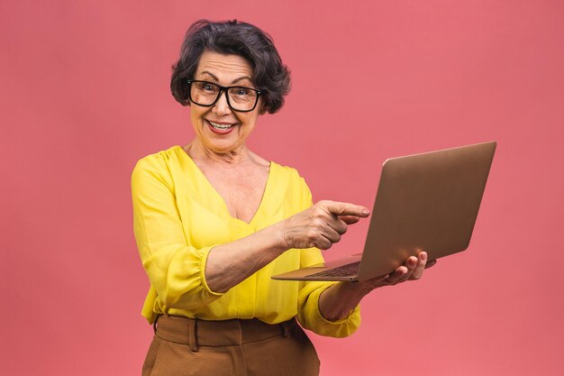 Donna d'affari anziana invecchiata con il portatile nonna isolata su sfondo rosa