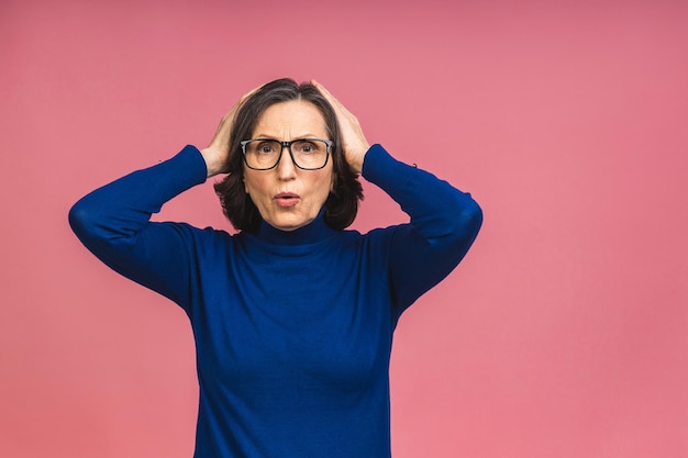 Senior aged pretty woman feeling shocked and excited, laughing, amazed and happy because of an unexpected surprise isolated over pink background.