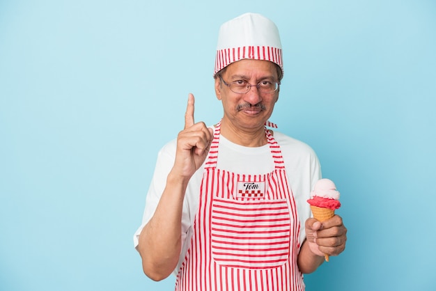 Senior american ice cream man holding an ice cream isolated on blue background showing number one with finger.