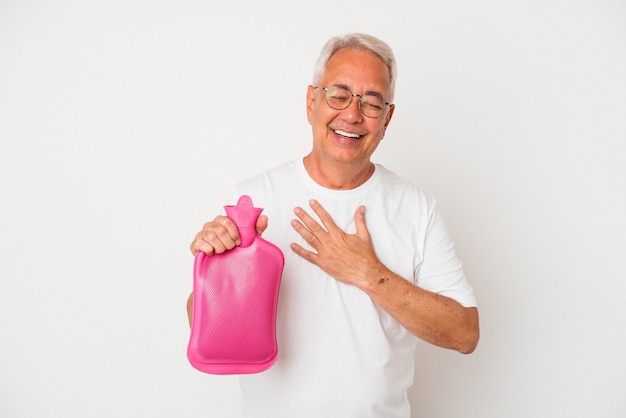 Senior american man holding a hot water bottle isolated on white background laughs out loudly keeping hand on chest.