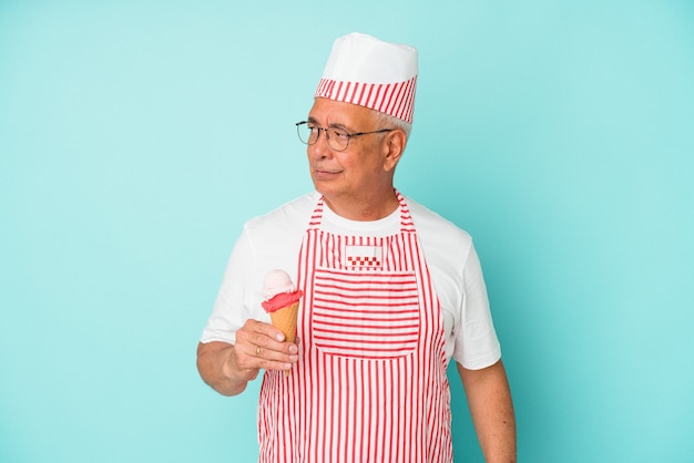 Foto senior amerikaanse ijsmaker die een ijsje geïsoleerd op een blauwe achtergrond verward vasthoudt, voelt zich twijfelachtig en onzeker.