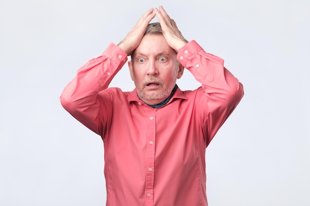 Senior angry man with hand at face on white studio wall