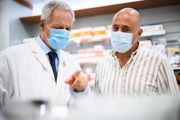 Senior apotheker die te maken heeft met een klant, beiden dragen maskers vanwege het coronavirus