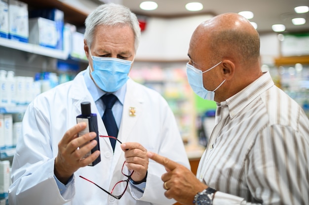 Senior apotheker die te maken heeft met een klant, die allebei maskers droegen vanwege het coronavirus