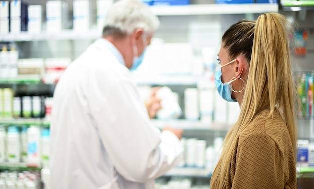 Senior apotheker die te maken heeft met een klant, die allebei maskers droegen vanwege het coronavirus