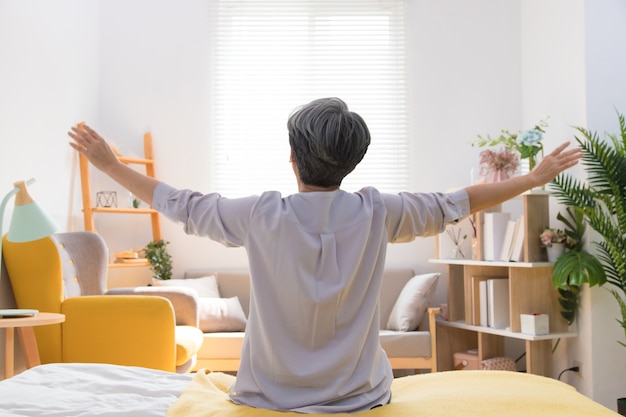 Senior Asia woman is sitting on the bed and stretch oneself in the morning at home