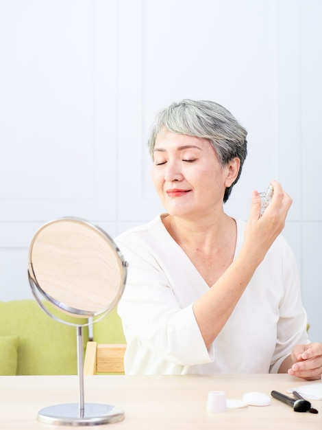 수석 아시아 여성이 집에서 향수를 뿌리고 있습니다.