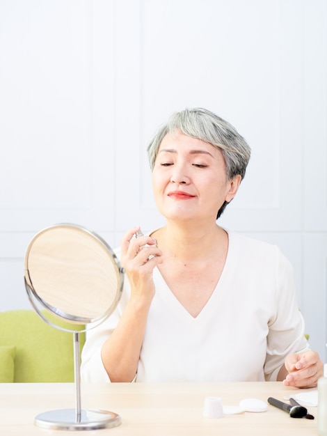 Senior Asia woman is spraying perfume at home.