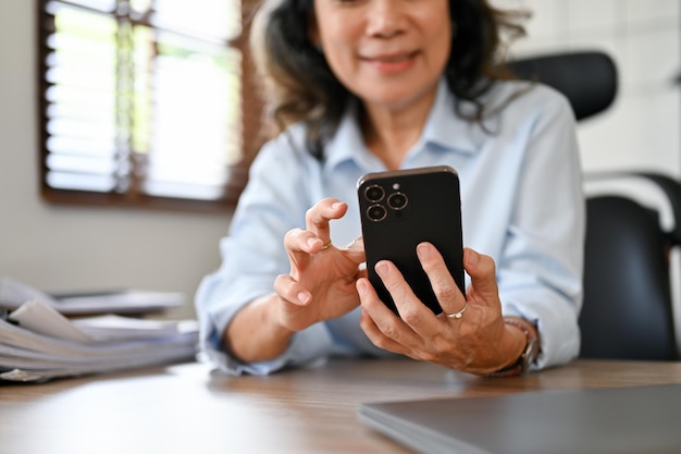 책상에 앉아 스마트폰을 사용하여 이메일이나 문자를 보내는 한 수석 아시아 여성