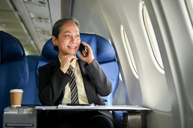 A senior Asian businesswoman is on the phone with her business partner during the flight