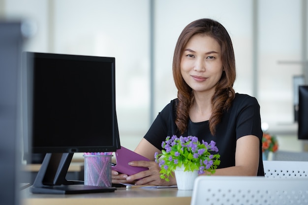 Senior Asian businesswoman sitting in office near computer screen and looking to camera with self confident.