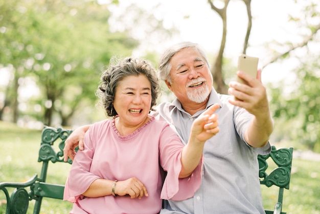 Coppie asiatiche senior che ridono e che sorridono insieme mentre esaminando smartphone