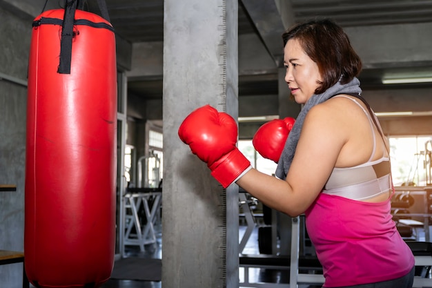 Pugilato grasso asiatico senior di addestramento della donna alla palestra di forma fisica.