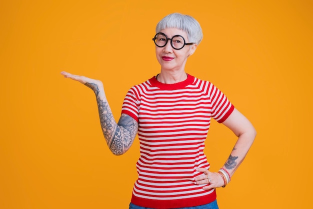 Senior asian female grey hair fashioned cloth with tattoo arm standing hand gesture with positive confident expressionold asia woman wear red tshirt carefree lifestyle happiness pension age