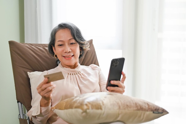 Senior Asian female using mobile banking application while relaxing in her living room