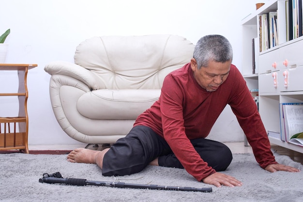 Senior Asian man falling down and lying on floor with wooden walking stick in living room