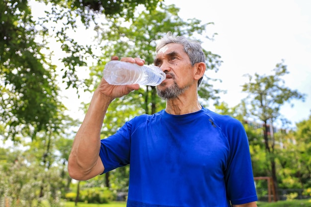 Senior Asian man is drinking water after morning exercise in the park for rehydration of sweat loss and healthy longevity lifestyle concept
