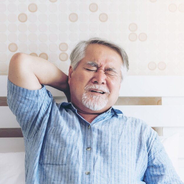 Senior Asian man , old man he wake up and sat on the bed , He had pain in the nape of his neck caused by sleeping on a pillow that is not correct posture - Senior people unhealthy diseased concept