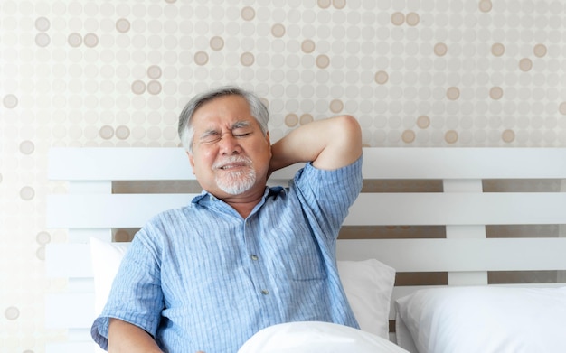 Senior asian man old man he wake up and sat on the bed he had\
pain in the nape of his neck caused by sleeping on a pillow that is\
not correct posture senior people unhealthy diseased concept