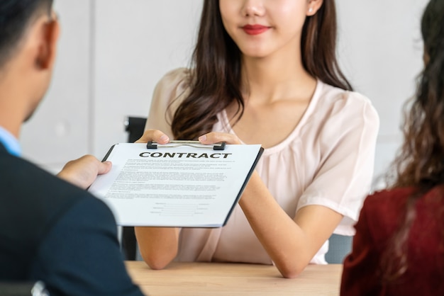 Senior Asian Manager submitting the contract document to Young Asian woman graduate