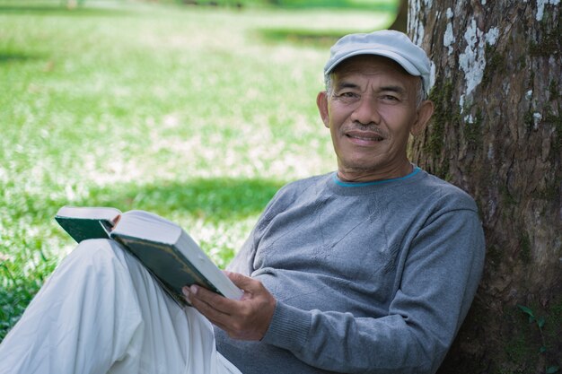 Uomo anziano asiatico senior che legge un libro all'aperto