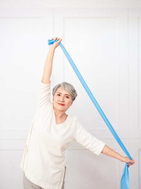 Senior asian woman doing exercises with resistance band at home.