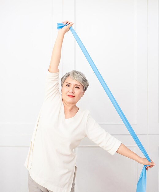 Senior asian woman doing exercises with resistance band at home.