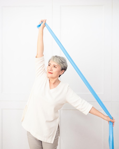 Senior asian woman doing exercises with resistance band at home.