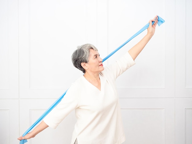 Senior asian woman doing exercises with resistance band at home.