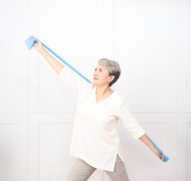 Senior asian woman doing exercises with resistance band at home.