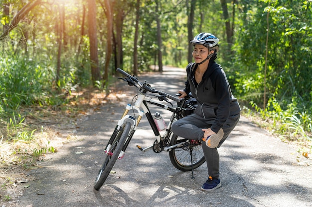 シニアアジアの女性は公園で自転車に乗って筋肉を伸ばす