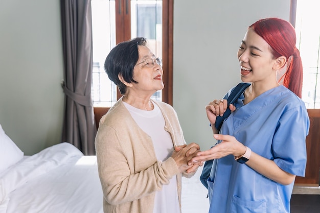 Senior Asian woman talking with Asian woman nurse wearing scrubs in the bedroom Caregiver visit at home Home health care and nursing home concept