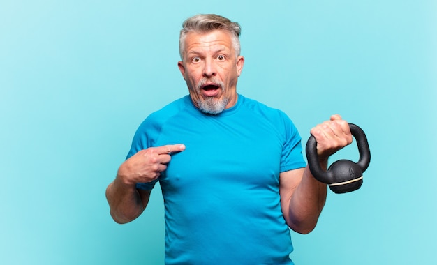 Senior athlete man looking shocked and surprised with mouth wide open, pointing to self