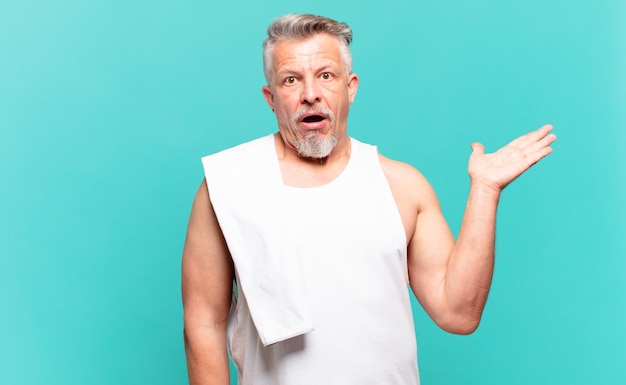 Senior athlete man looking surprised and shocked, with jaw dropped holding an object with an open hand on the side