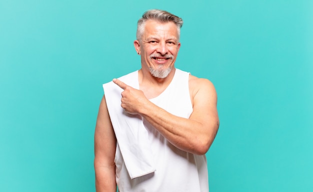 Senior athlete man smiling cheerfully, feeling happy and pointing to the side and upwards, showing object in copy space