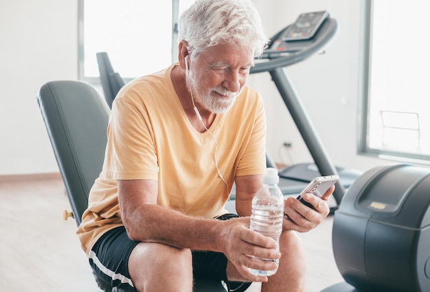 Senior athletic man takes a break in the gym between exercises uses mobile phone Sport gym concept