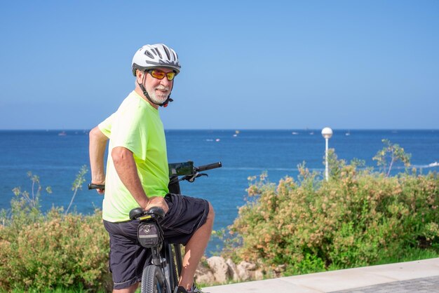 健康的なライフスタイルを楽しむ海での屋外遠足で電動自転車を持つシニア運動男性