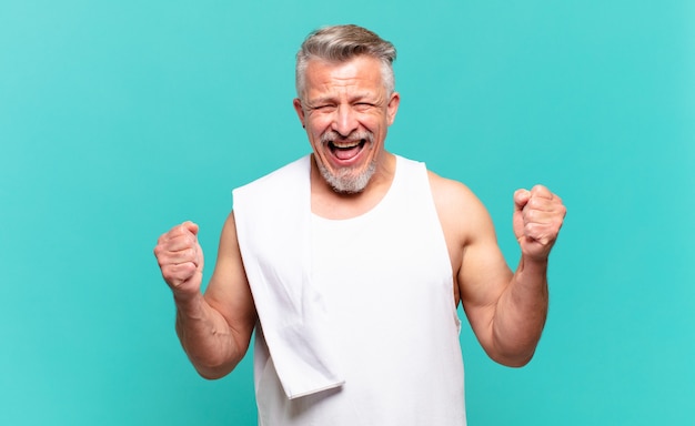 Senior atleet man voelt zich geschokt, opgewonden en gelukkig, lacht en viert succes en zegt wow!