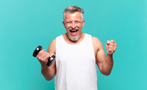 Senior atleet man voelt zich geschokt, opgewonden en gelukkig, lacht en viert succes en zegt wow!