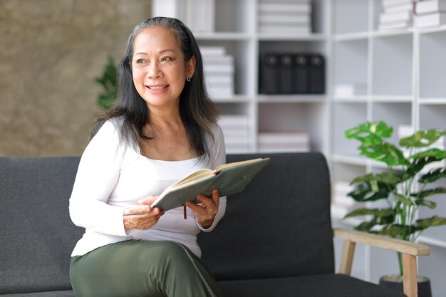 Senior Aziatische vrouw die een boek leest en ontspant op de bank thuis