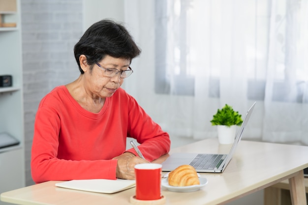 Senior Aziatische vrouw ontspannen met behulp van laptopcomputer zittend op tafel.